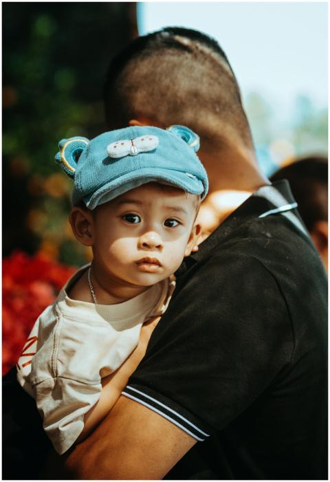 A father carrying his baby in a blue hat on a sunn