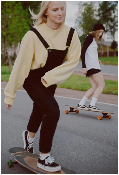 Two women riding longboards in a park, enjoying a