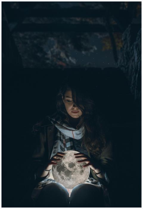 A woman holds a glowing moon orb in a dark, atmosp