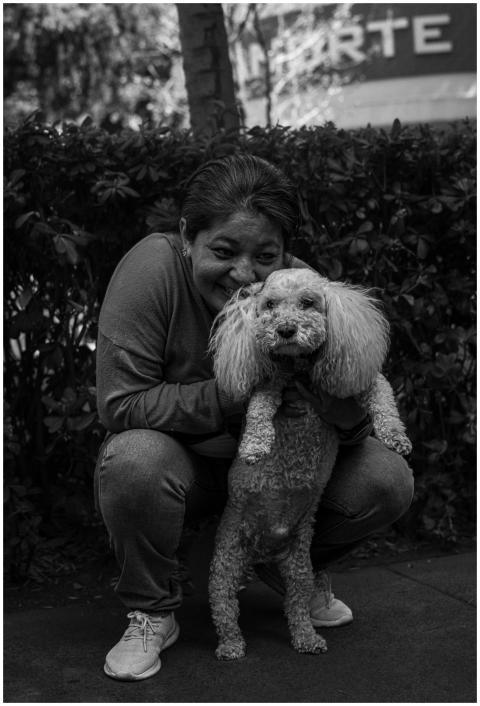 A woman smiles while crouching with her poodle in