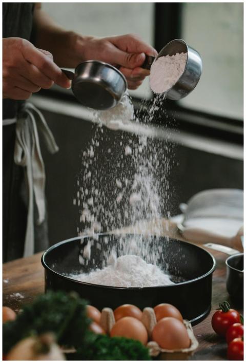 Crop anonymous chef pouring flour into baking dish