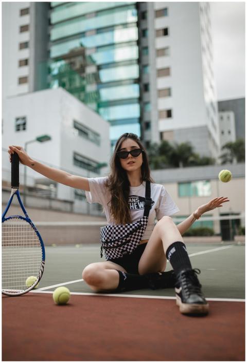 Stylish woman in sunglasses posing with tennis rac