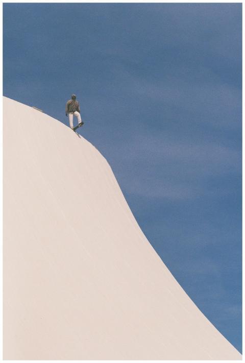 A skateboarder stands atop a white hill with a bri