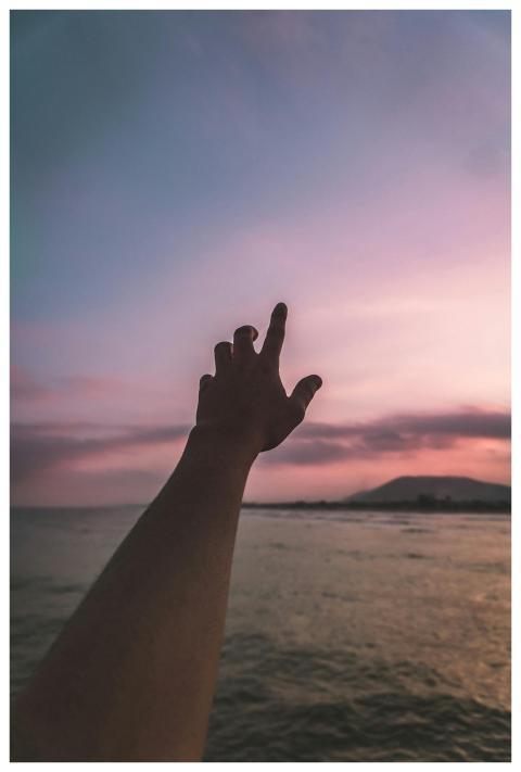 A silhouetted hand stretches upward against a colo