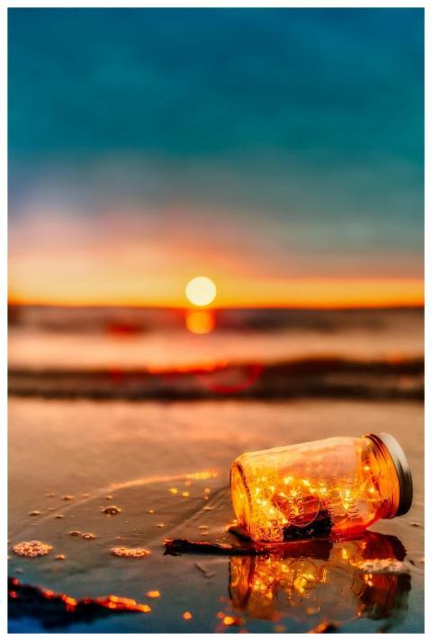 A lit jar with lights sits on a beach, creating a