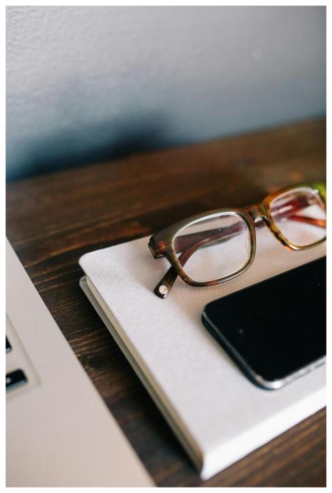 A close-up of a desk with a smartphone, eyeglasses