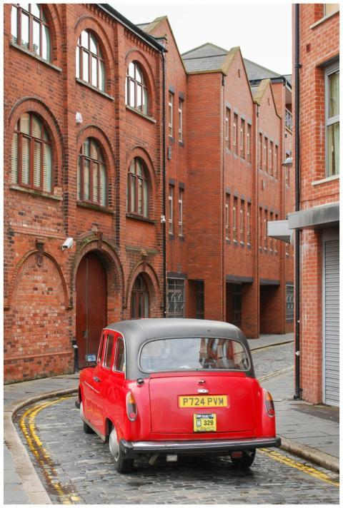 A classic red vintage car on a narrow cobblestone