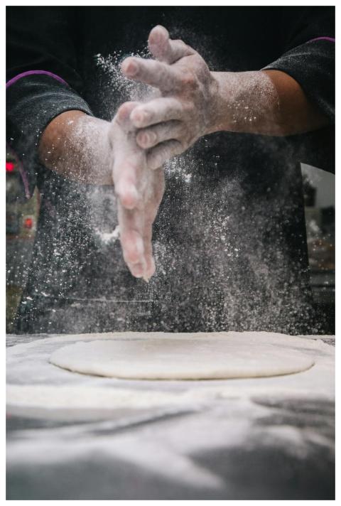 A chef clapping hands over dough, releasing flour
