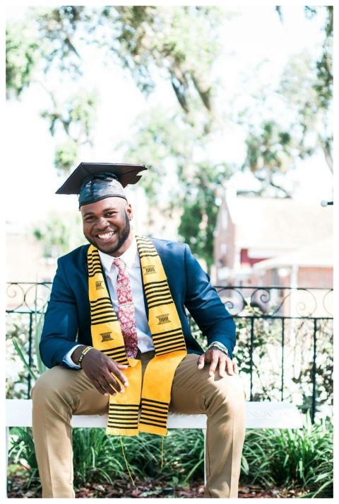 Smiling graduate sitting outside wearing a cap and