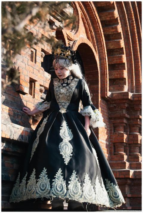 Woman in ornate black and gold gown standing by a