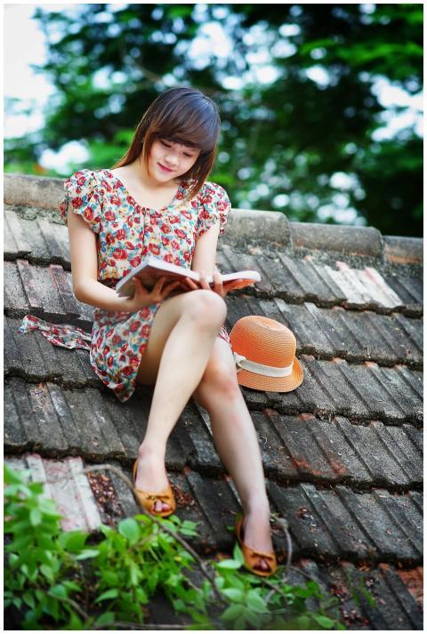 Cheerful young woman in a floral dress reading a b