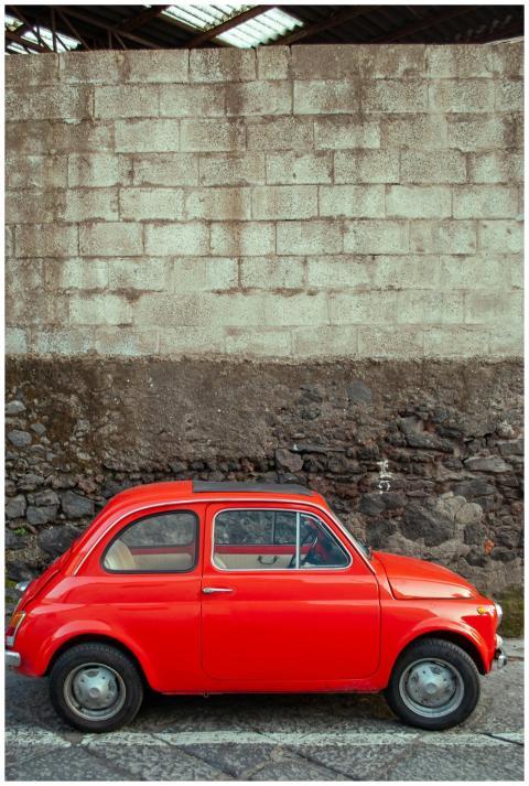 Classic red Fiat 500 parked against a rustic wall