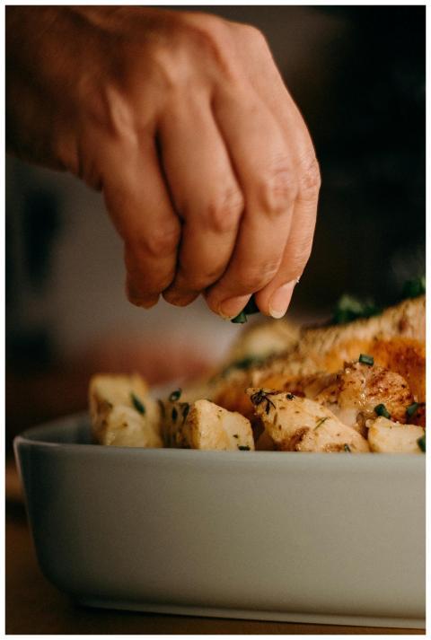 Close-up of a chef's hand garnishing roasted potat