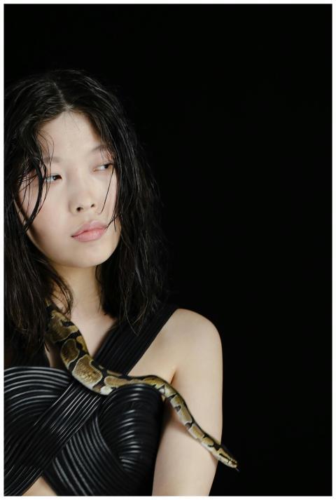A woman poses with a snake against a dark backgrou
