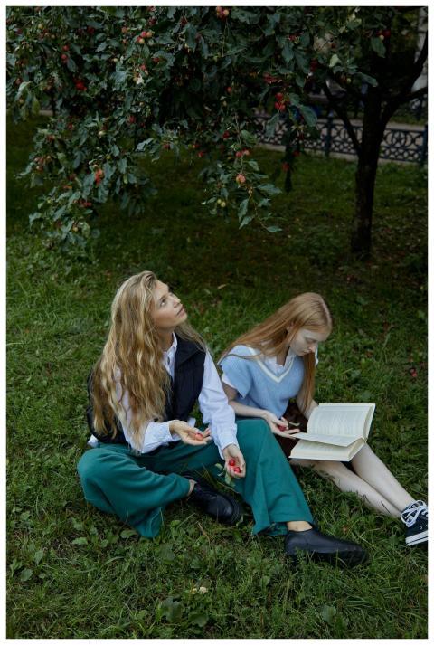 Two women sitting under a tree, one reading a book
