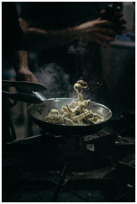 Chef skillfully tosses pasta in a steaming pan, sh