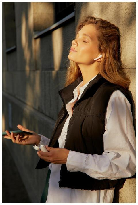A woman in a black vest enjoys music with earphone