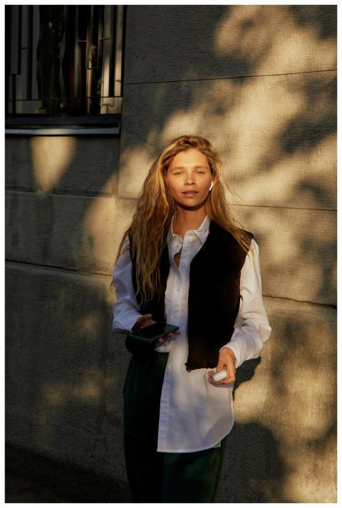 Woman holding phone and earphones, standing by a c