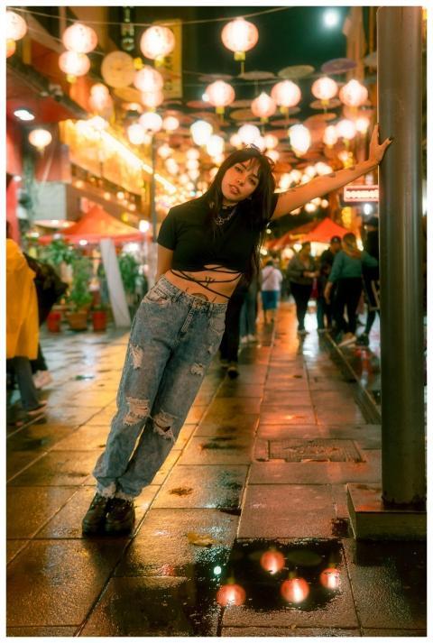 A young woman poses under festive string lights in
