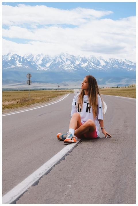Woman sitting on rural road with scenic mountain b