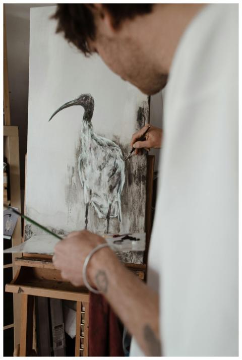 A dedicated artist painting an ibis bird on canvas
