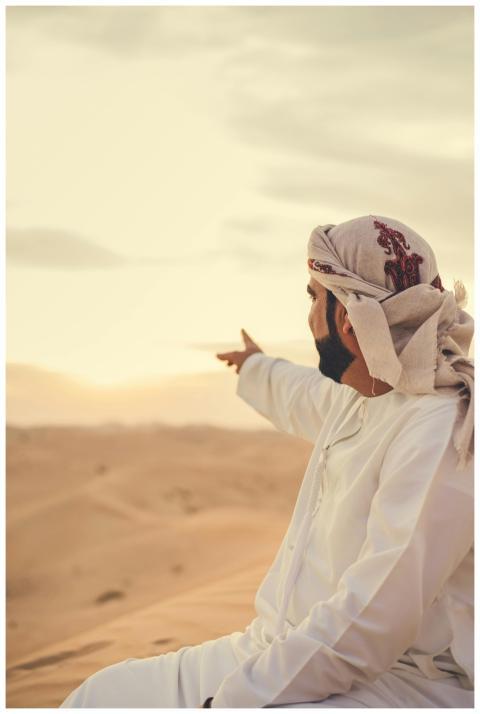 A man wearing a thawb and headscarf points across