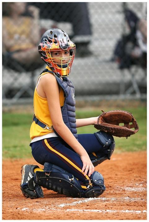 Young female softball catcher in full gear ready i