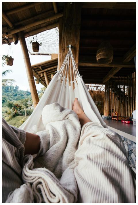 Crop barefoot traveler chilling on white cozy hamm