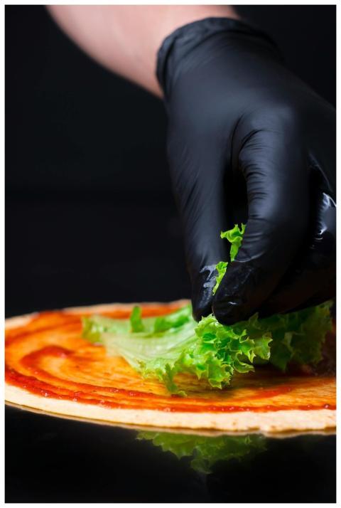 Close-up of a gloved hand placing lettuce on pizza