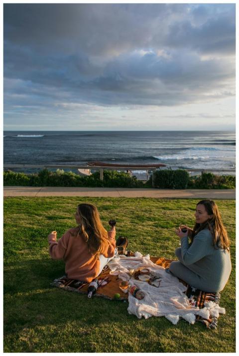Two women enjoying a seaside picnic, embracing a p