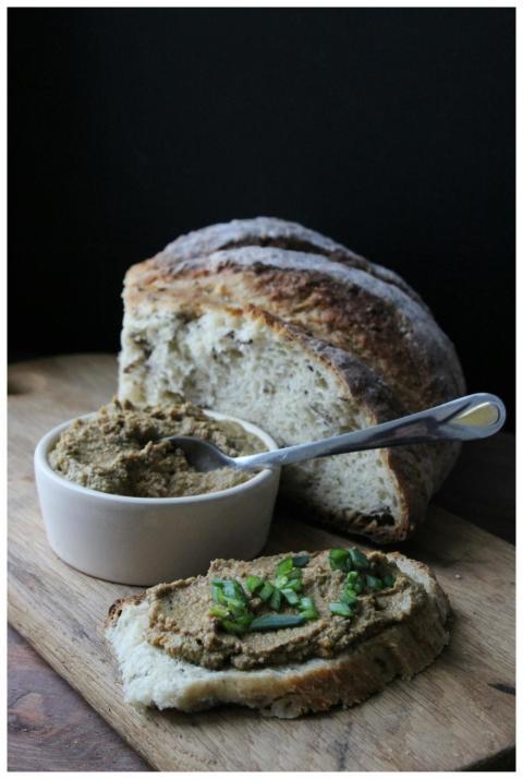 A rustic loaf with savory spread garnished with sp