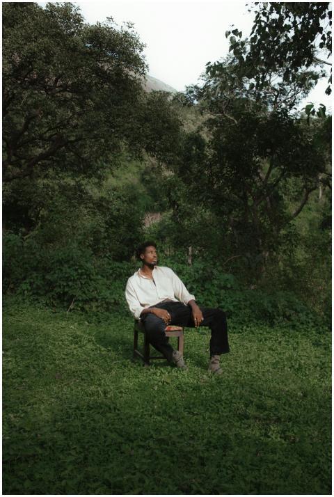 A man in casual attire sits on a chair in a serene