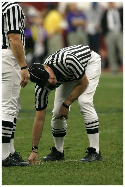 Football referee bends down to measure the yard li
