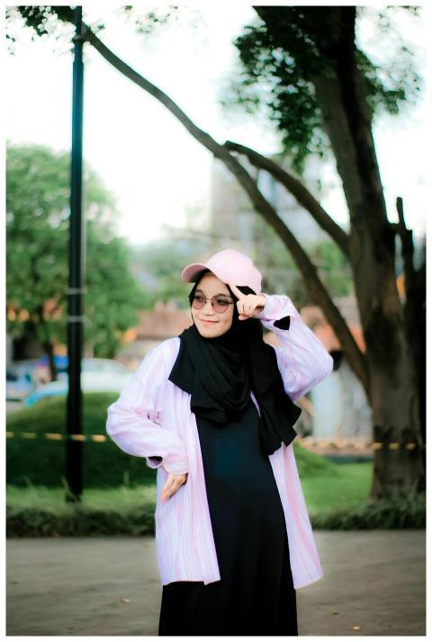 Young woman in stylish attire posing in a lush, gr