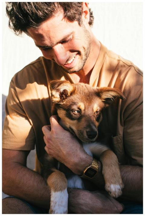 Smiling man embraces a cute puppy outside on a sun