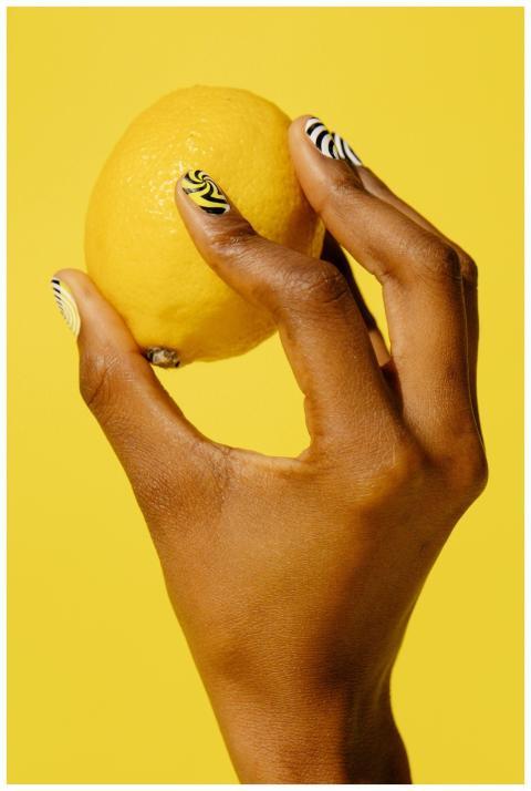 Close-up of lemon held by hand with artistic nail