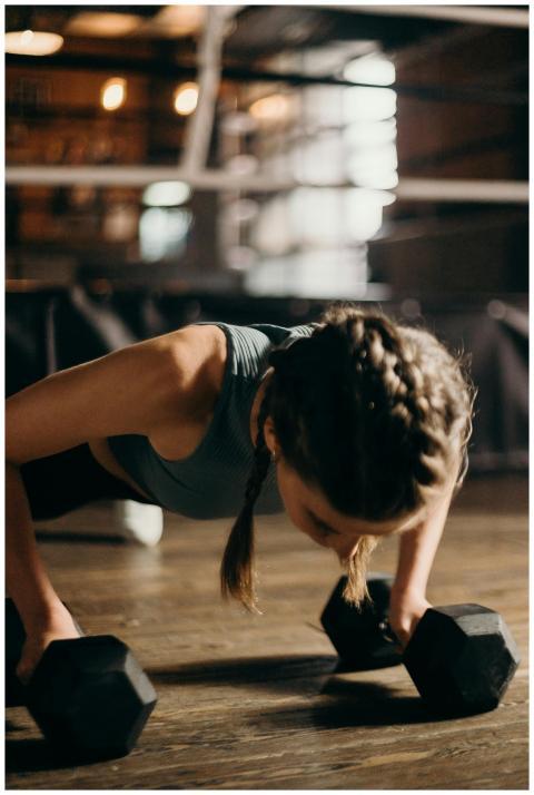Fit woman doing push-ups with dumbbells indoors, e