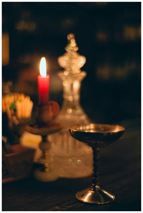 Flaming wax candle near crystal decanter and golde