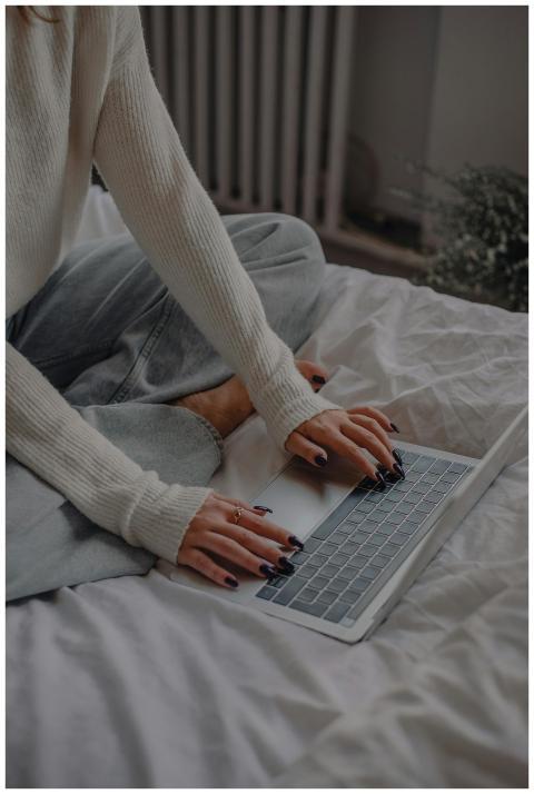 A woman with painted nails sitting on bed, using a