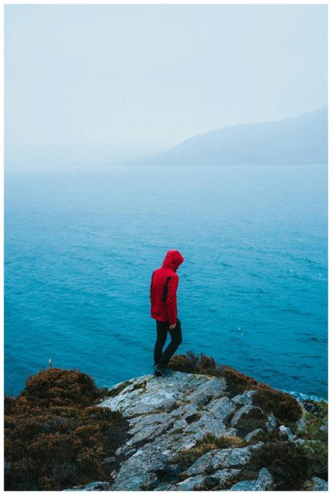 Lone person in red jacket on a foggy cliff in the