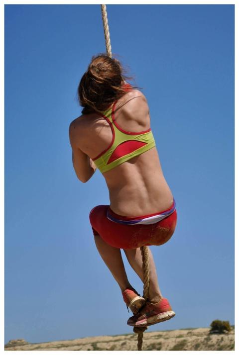 A fit adult woman in athletic wear climbs a rope o