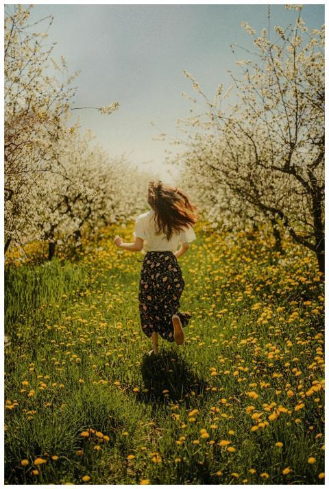 A carefree young woman runs through a meadow of bl