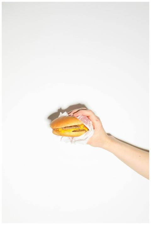 A close-up of a cheeseburger held by a hand on a w