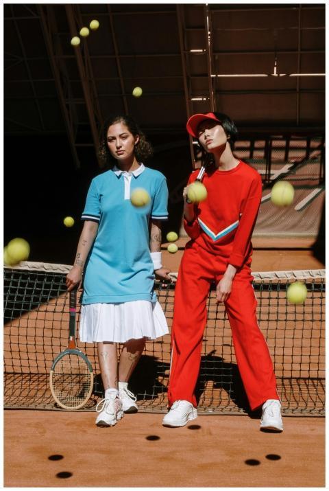 Two women pose on a tennis court amidst bouncing b