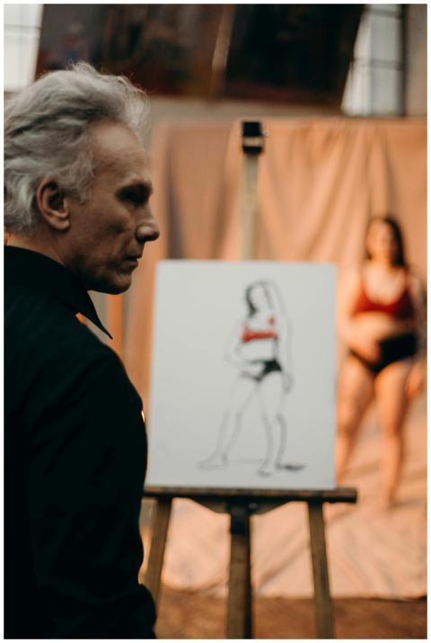 Male artist sketches a female model in a dimly lit