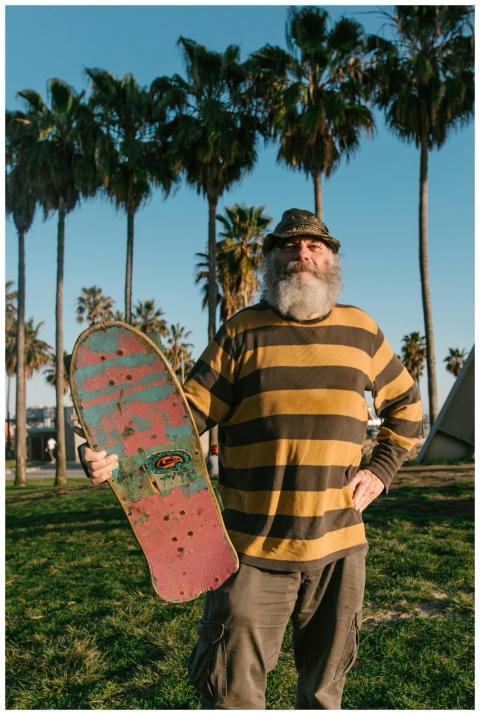 Bearded elderly man holds skateboard in sunny park