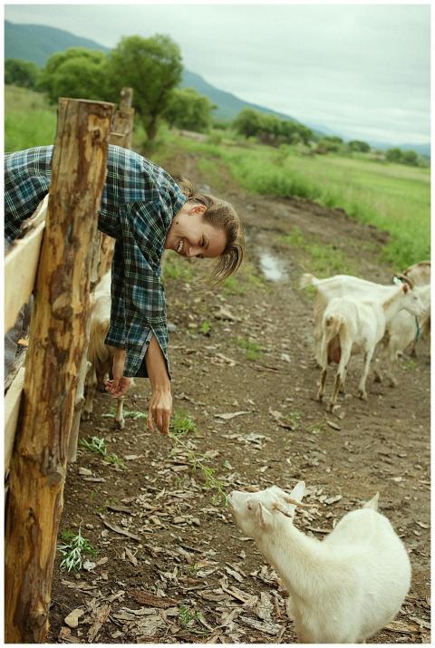 Smiling woman in plaid shirt feeds goats through a