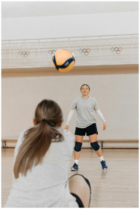 Two female athletes practicing volleyball indoors,