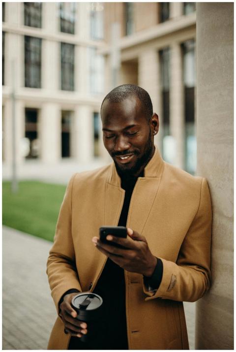 Relaxed man in coat smiles while using smartphone