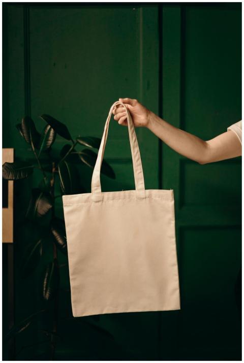 Simple cotton tote bag held by a hand against a gr